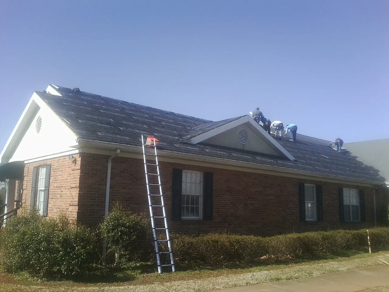 Crew tearing shingles off a brick ranch roof with a ladder set — Emergency Roof Repair work by our crew in Bally