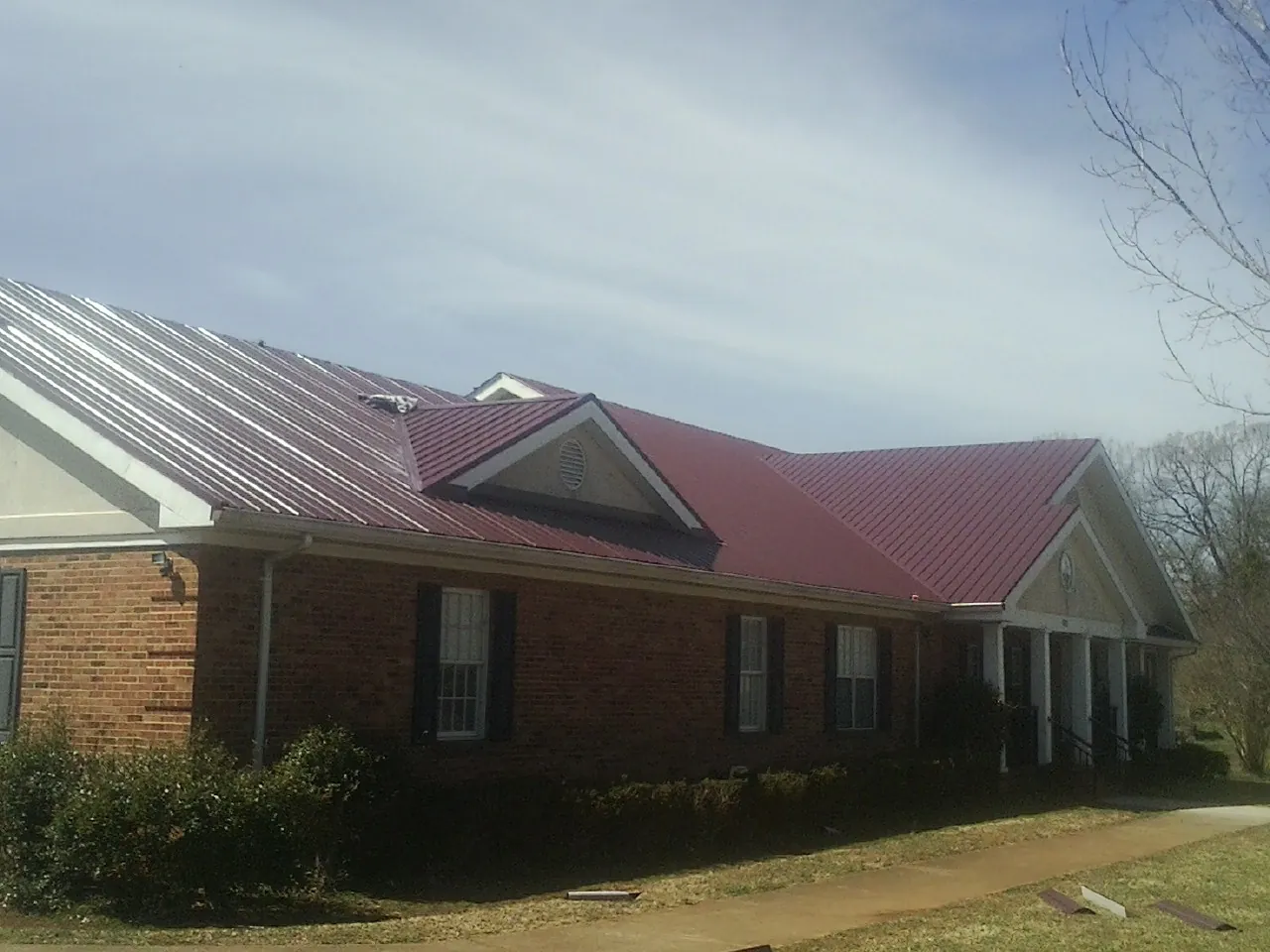 Red metal roof with gabled entries on a long brick building, from a Hail Damage Roof Repair job in Bally
