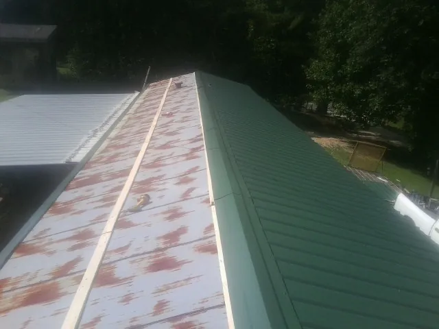 Old rusted panels beside newly installed green metal roofing — Wind Damage Roof Repair by Roofing Brothers in Bally