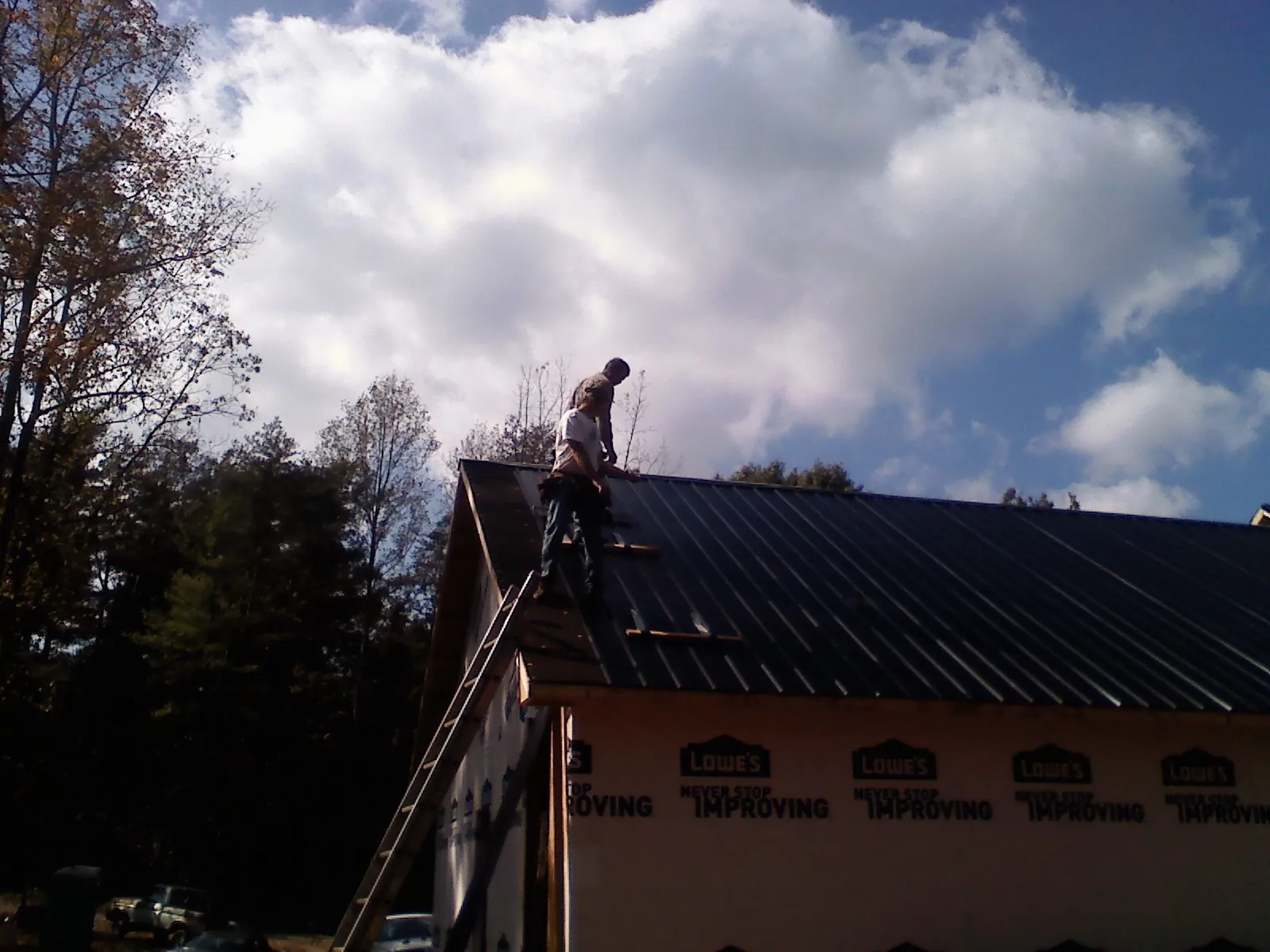 Roofer fastening dark metal panels high against a cloudy sky, from a Roof Inspection job in Bally