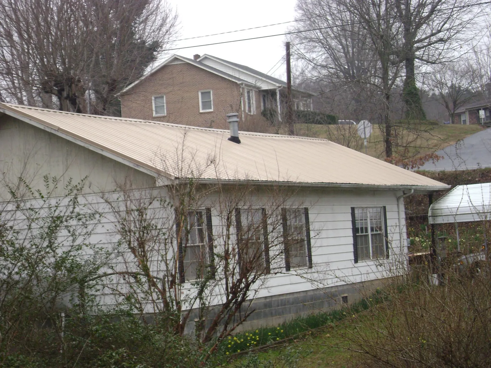 Tan metal roof on a white sided house set into a hillside — Commercial Roofing by Roofing Brothers in Bally
